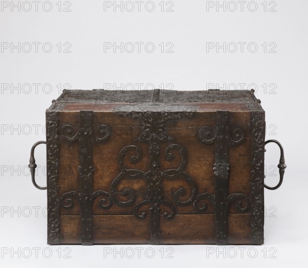 Cabinet, late 17th century, Northern Germany, or Poland, cuboid storage piece height 70.1 cm, width 89.2 cm, depth 55.9 cm. Cabinet with a drawer at the top and double doors below, richly decorated with openwork engraved fittings with grotesque motifs, wickerwork ornament, fantastic animals and figures, plant tendrils, and male figures. The inner door leaves are veneered with rosewood and ebony in geometric arrangements, divided by inlaid bone veins, with figures in engraved bone signed Hippocrates on the left and Hermes on the right. Behind the doors are twelve compartments. Drawer and door locks have engraved steel plates; the drawer lock blocks the left door leaf. Steel hinges., A wooden chest with dark brown tones and a weathered surface is shown, featuring ornate black metal straps and decorative scrollwork across its front and top, and a curved metal handle on each side that are dark gray to black in color; the background is a plain light gray to white.