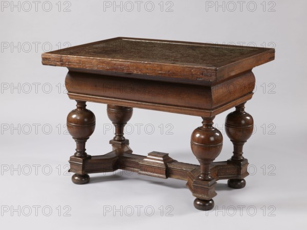 Stock exchange table, provenance unknown, Baroque, stone tops, rectangular. Rectangular stock exchange table with a stone top enclosed in a wooden frame and a drawer in a high frame, supported by four turned baluster legs joined with an H link made of profiled beams. Baluster legs with massive balls in the upper section, terminating at the bottom with flattened balls. In the central section of the link, a rectangular extension with a pinnacle not preserved. Reinforcing parquetry under the top. Applied drawer bottoms with slides. Stone top polished only on the upper surface. Drawer lock plate in the form of a cartouche topped with a lily. Steel lock, mortise-and-slip, double-bolt. 4th quarter of the 17th century, Royal Prussia, furniture, table. Dimensions: height 88.5 cm, width 121.3 cm, depth 90.4 cm., A wooden table with a rectangular top and a darker inset surface sits against a plain light gray background. The table is finished in brown tones with visible wood grain and worn areas ...