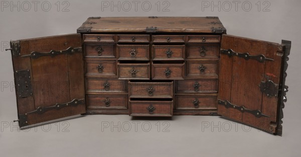 Cabinet, Baroque, 2nd quarter of the 17th century, Gdansk. A cuboid cabinet with a boarded body, fitted with steel decorative strips, closed with double doors. Framed doors with single panels in the form of convex coffers glued at the mitre from richly profiled strips. Steel closing strip with a wavy outline; rectangular and trefoil-shaped angular fittings on the edges of the body, punched, fastened with headers. Inside, sixteen drawers arranged in five rows: two in the top, four in each of the two middle rows, three in the bottom row. Drawer faces are framed with profiled strips; the three drawers in the middle row feature numerous internal divisions. Walls connected with exposed diagonal dovetails; back joined to top and sides with dowels. Drawers have exposed diagonal dovetail joints; bottoms are nailed. Side handles are oval; drawer handles are round with rosette-shaped plates. Hinges are steel, strap-type, with a wavy outline. Both door leaves have steel mortise-and-apply locks wi...