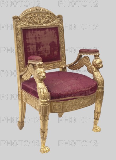 Armchair, unknown creator; ; griffins; Empire style; braids; grotesques ornament; birds; kimation ornament; plant decoration; vase ornament; early 19th century, Europe; piece of furniture, seating piece; height 108 cm, width 69 cm, depth 54 cm., A carved wooden chair with a gilded finish and a deep red velvet upholstered backrest and seat, the back framed by ornate floral and scrollwork carvings and topped with a rounded crest, the armrests ending in carved winged animal heads supporting small padded rests covered in matching red velvet, the seat cushion showing textured wear, the apron around the seat decorated with carved medallions and floral motifs, the front legs carved with fluted and foliate details terminating in paw-shaped feet, and the overall colors visible are gold and deep red, set against a plain light gray background.