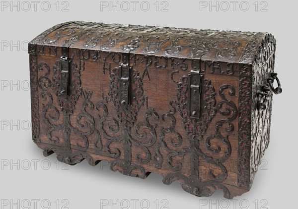 Chest, provenance unknown, Baroque style. Acanthus twig and plant decoration, fantastic figures, monograms. Bottle-shaped with a convex lid, side walls slightly tapering toward the bottom. Decorated with openwork; repoussé fittings with plant motifs; supported by four steel rings covered on the long sides with wavy aprons. On the lid, three forged strips extending from the front into the lock hasps and strap hinges; between them the forged date ANNO 1704 DEN 3 MAJ. Below, on the front wall of the body, the monogram BH AC / WZ LS. Front features lock plates transitioning to aprons bearing the wheel axles at the bottom. Edges fitted with openwork steel bands with plant twig motifs. Sides with two pull handles. Walls and lid joined with exposed diagonal dovetails. Interior lined with paper no print and canvas. Webbing straps attached to the sides to hold the lid open. Mortice-type locks with elongated rectangular key covers with a knob. Dated to the 1st quarter of the 18th century, possib...