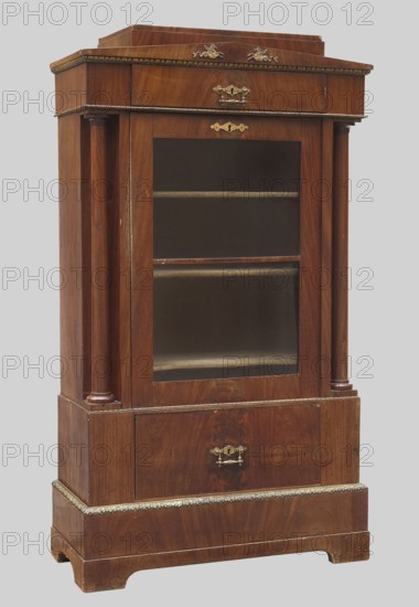 Library cabinet, fantasy animals, columns, Biedermeier style, egg-shaped ornament, cabinet with straight sides and front, with a drawer at the top and bottom, single-leaf, supported by a high plinth with console legs. Entire unit veneered with mahogany. Columns in the front corners. Door leaf glazed, divided into two sections by a horizontal muntin. Finial features a triangular, flattened pediment and a stepped, two-stage canopy. Crowning cornice features a gilded egg-shaped pediment. Pediment features brass appliqués — two seahorses and a Medusa head missing. Three shelves inside. Steel pintle hinges. Mortise-type locks, single-bolt, with steel plates. Other fittings combined handle and lock plates not original. 1830–1840, Germany. Furniture; storage furniture. Height 167 cm, width 96.5 cm, depth 41 cm., A wooden display cabinet with a polished brown finish and visible wood grain, featuring a glass-fronted central section with a few interior shelves, a lower drawer, and decorative met...