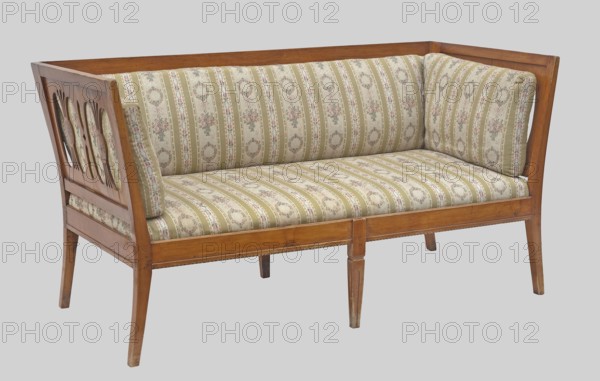 Sofa, unknown origin, Biedermeier, epergne ornament, classicism; arched outer legs and straight middle ones with a groove. Backrest with two horizontal slats, the upper one wider. Openwork sides composed of a motif of four kidneys separated by arched muntin bars. Backrest and side cushions are overlaid; inset seat. 1815–1825, Central Europe. Piece of furniture seating, H 81 cm × W 157 cm × D 74.9 cm., A wooden framed loveseat with a patterned upholstered seat and back cushions, the wood showing a medium brown finish and the fabric featuring a striped floral motif in shades of beige, green, cream, pink, and muted red, with carved circular cutouts on the wooden side panel and tapered wooden legs in a medium brown tone.