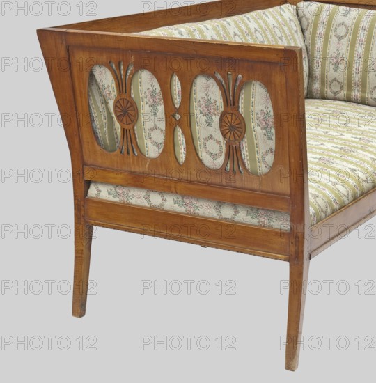 Sofa, origin unknown, Biedermeier, epergne ornament, classicism. Arched outer legs, straight middle ones with a groove. Backrest with two horizontal slats, upper one wider. Openwork sides composed of a motif of four kidneys separated by arched muntin bars. Backrest and side cushions overlaid, inset seat. 1815–1825, Central Europe. Piece of furniture seating, H 81 cm, W 157 cm, D 74.9 cm., A wooden upholstered bench or settee shown from an angled side view with a carved wood frame featuring oval cutouts filled with patterned fabric; the wood is a warm brown with visible grain and some wear at edges. The upholstery fabric has a floral and striped pattern in soft colors including green, cream, pink, and pale blue. The seat cushion and backrest are covered in the same patterned fabric, and a narrow upholstered panel runs along the lower front. The carved wood details include radial rosette motifs and elongated cut shapes. The floor or background appears pale gray.