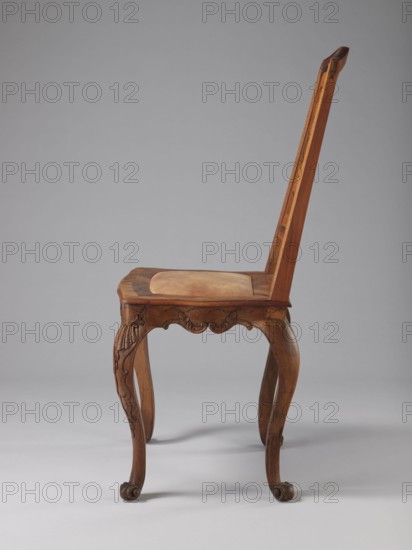 Chair, creator unknown, origin Germany, Rococo style, ca. 1750–1765. Rococo chair with a boarded inlaid backrest depicting a lady in a crinoline surrounded by flowers; rectangular originally upholstered seat; supported by cabriole legs decorated in bas-relief with motifs at the top including shells on the knees and terminating in volute feet. Frame has a wavy-cut bottom decorated with acanthus leaves. Seat frame with a wavy outer outline enclosing a padded central section. High backrest with clearance, angular stiles, and a wavy-curved upper section. Inlaid representation on the backrest framed by two intertwining U-shaped ribbons. Ornamentation includes volutes, plant decoration, acanthus, shells, female figures, flowers, and ribbon-and-pincer motifs. Seating piece, height 115 cm, width 53 cm, depth 63 cm., The image shows a wooden chair photographed from the side against a gray background, featuring a tall, straight back and a seat with an upholstered cushion in a light tan color; th...