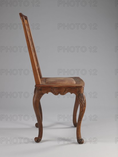 Chair, origin unknown, Rococo style, volutes, plant decoration, acanthus, shells, female figures, flowers, ribbon-and-pincer ornament. Rococo chair with a boarded inlaid backrest a lady in a crinoline surrounded by flowers, a rectangular originally upholstered seat, supported by cabriole legs. Legs decorated in bas-relief with motifs at the top, including shells on the knees, terminating in volute feet. Frame wavy-cut at the bottom, decorated with acanthus leaves. Seat frame with a wavy outer outline enclosing a padded central section. High backrest with a clearance, angular stiles, and a wavy-curved upper section. Inlaid representation on the backrest framed by two intertwining U-shaped ribbons. Ca. 1750–1765, Germany. Piece of furniture, seating piece. Height 115 cm, width 53 cm, depth 63 cm., A wooden chair shown in profile with a tall slanted backrest and a flat seat topped by a padded cushion, all in shades of brown; the backrest and seat frame display carved decorative details, a...