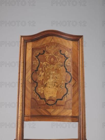 Chair, origin unknown, Rococo style, ca. 1750–1765, Germany. Rococo chair with volute and shell ornamentation, plant decoration including acanthus, female figures, flowers, and ribbon-and-pincer motifs. Boarded inlaid high backrest showing a lady in a crinoline surrounded by flowers, framed by two intertwining U-shaped ribbons. Rectangular originally upholstered seat supported by cabriole legs decorated in bas-relief with motifs at the top shells on the knees terminating in volute feet. Wavy-cut lower frame decorated with acanthus leaves; seat frame with wavy outer outline enclosing a padded central section. Backrest has a clearance, angular stiles, and a wavy-curved upper section. Piece of furniture seating, height 115 cm, width 53 cm, depth 63 cm., A wooden chair back with a curved top and a rectangular inset panel featuring a decorative marquetry scene; the wood shows warm brown and honey tones with darker brown grain and black inlaid accents; the central inlaid design depicts a sea...