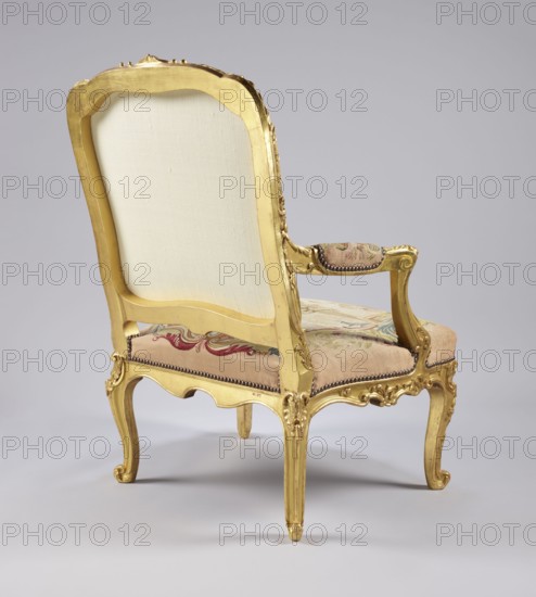 Armchair, attributed to Jean-Baptiste Oudry 1686–1755 and unknown co-creator; carved, gilded, and upholstered seating piece in the Rococo à la reine style. Tapestry upholstery Aubusson and/or Beauvais? depicting scenes from Jean de La Fontaine's fables framed with flowers: backrest shows an insect nest in a landscape — illustration of the tale The Hornets and the Bees — and the seat shows The Wolf and the Lamb wolf and lamb by a stream. Upholstery includes wolves, lambs, plant decoration, insects, flowers, bees. Cabriole/S-shaped legs with acanthus-shaped volute feet; backrest roughly rectangular with slightly concave side rails, convex top and rounded corners; trapezoidal seat with slightly bulging frames; recessed, volute-topped armrests on U-shaped supports. Carved floral ornamentation with acanthus leaves, shells, rocaille elements and rose clusters. 3rd quarter of the 18th century, France. Dimensions: height 106.5 cm, width 77.5 cm, depth 79.4 cm., A decorative upholstered chair s...
