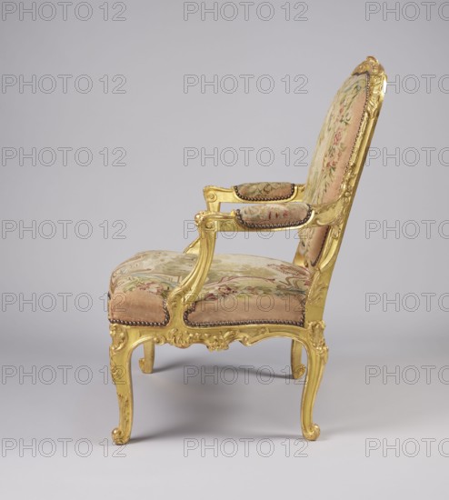 Armchair by Jean-Baptiste Oudry 1686–1755 and unknown co-creator; carved, gilded, and upholstered à la reine-style Rococo armchair seat, backrest, and armrests with tapestry upholstery featuring scenes from Jean de La Fontaine's fables framed with flowers. Backrest depicts an insect nest against a landscape illustration of the tale The Hornets and the Bees; seat depicts a wolf and a lamb by a stream The Wolf and the Lamb. Design details: backrest roughly rectangular with slightly concave side rails, convex top, rounded corners and clearance; trapezoidal seat with slightly bulging frames; recessed, volute-topped armrests resting on U-shaped supports; S-shaped legs with acanthus-shaped volute feet. Carved floral decoration with acanthus leaves, shells, flowers, rocaille elements and bunches of roses. Rococo style, 3rd quarter of the 18th century, France. Upholstery possibly Aubusson or Beauvais. Furniture type: seating piece. Dimensions: height 106.5 cm, width 77.5 cm, depth 79.4 cm., Th...