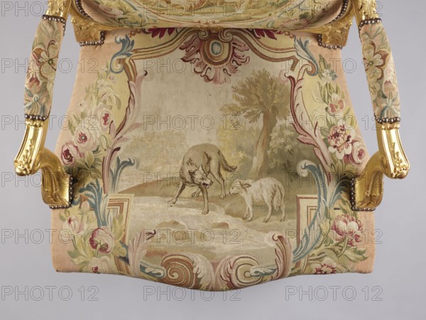 Armchair, attributed to Jean-Baptiste Oudry 1686–1755 and an unknown co-creator; carved, gilded, and upholstered Rococo armchair in the à la reine style. Tapestry upholstery Aubusson and/or Beauvais? featuring scenes from Jean de La Fontaine's fables framed with flowers: backrest depicts an insect nest in a landscape illustration of The Hornets and the Bees, seat depicts The Wolf and the Lamb by a stream. Decorative motifs: wolves, lambs, insects, flowers, bees, plant decoration, shells, rocaille elements, acanthus leaves, bunches of roses. Form: roughly rectangular backrest with slightly concave side rails, convex top and rounded corners; trapezoidal seat with slightly bulging frames; recessed, volute-topped armrests on U-shaped supports; S-shaped cabriole legs with acanthus-shaped volute feet. Function: seating piece. Date: 3rd quarter of the 18th century. Place of origin: France. Dimensions: height 106.5 cm; width 77.5 cm; depth 79.4 cm., A decorative upholstered chair seat seen fro...