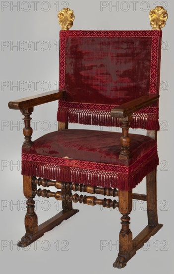 Armchair, animal paws, feathers, pre-war collection, upholstered. ARMCHAIR rectangular seat and backrest, with turned and angular structural elements. Legs mounted on runners terminating in animal paws at the front; the front legs transition into turned armrest supports, with cubes at the joints with the ties, frames, and armrests; the rear legs, together with the side rails of the backrest, are angular. Legs joined in pairs by ties – two turned ones at the front, one angular at the back. Flat, angular armrests, finished with a volute at the front and chamfered on the outside. The backrest is slightly tilted back, with a clearance, and the side rails are finished with carved, gilded pinnacles in the shape of volute-shaped acanthus leaves. The whole is upholstered in red silk velvet, finished with a silk ribbon with a geometric pattern, with a fringe at the bottom of the backrest and around the seat. Armchair of the poltrona da parata type, 16th–17th century, Italy, possibly Venice; sea...