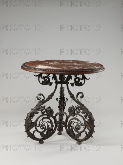 Table, Szewczykowski, Roman 1849–1901 creator, plant decorations, plant twig, astragal, in the form of three S-shaped pieces, 1890s, Warsaw, furniture, table, height 80.7 cm, diameter 84 cm, An ornate round table with a reddish-brown marble top showing lighter veining and a carved wooden edge sits on an intricately carved dark wood base; the base features scrolling foliate and acanthus motifs forming symmetrical curved supports with spherical accents and a central carved column, all set against a light gray background.