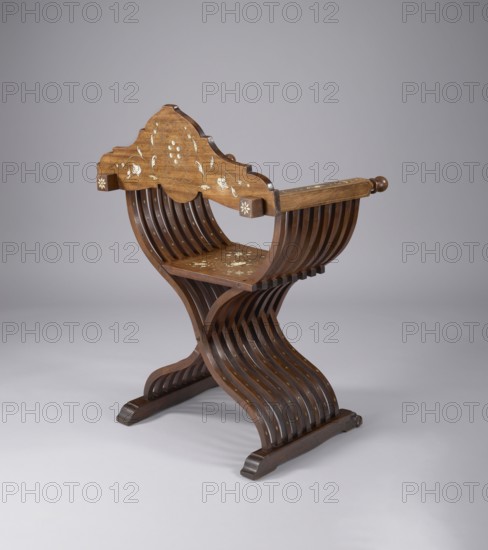 Scissor chair, Scissor armchair made of eight pairs of crossed S-shaped slats, connected at the bottom by runners and at the top by armrests, with a board backrest and seat, decorated with ivory inlay. The slats are fastened with a steel rod at the intersection, which, together with the lifting seat and backrest board, enables the structure to be folded and unfolded. The runners are angular, ending in carved animal paws at the front. The armrests are angular, ending in spheres and movable rings. The backrest is roughly triangular in shape, with a wavy outline, and the seat features an apron added at the front. The backrest board features an inlaid Medici coat of arms beneath a seven-baton crown, supported by putti and lions. Decoration around and on the seat is a grotesque twig; the slats are inlaid with rhombuses and further ornamented with crowns, coats of arms, lions, putti, plant twigs, grotesques, cartouches, rosettes, and mascarons. Neo-Renaissance style. Third quarter of the 19t...