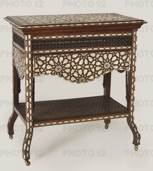 Side table, Rectangular side table with drop-down desks on each side and a bottom shelf, inlaid with mother-of-pearl and bone in geometric and plant patterns. Straight, angular legs that are S-shaped at the bottom and topped with brass rollers. Wide openwork frame filled with a dense lattice of turned elements mashrabiya. Tabletop, desks, frame, and shelf edge decorated with geometric braid forming rosettes; shelf covered with stars with hexagonal fields forming a network. Desk supports imitate bamboo. 19th century, 2nd half; Syria . Furniture, table. Dimensions: height 82 cm, width 100 cm, depth 75 cm., A wooden side table with decorative inlay in cream and dark brown forming geometric star and lattice patterns on the top, apron, legs, and sides; the table has a rectangular top, a scalloped apron panel with geometric inlay, a lower shelf with a dark patterned surface, turned wooden supports beneath the apron, and cabriole-style legs ending in small brass casters.
