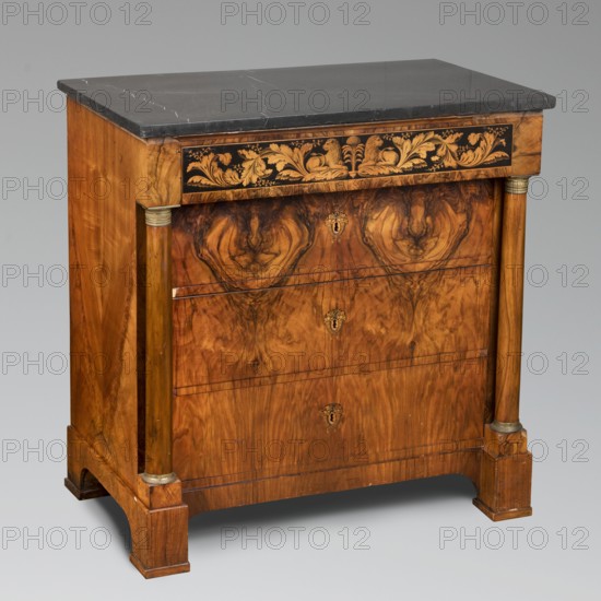 Chest of drawers, Biedermeier style, ca. 1820, Southern Germany possibly Munich. Cuboidal four-drawer chest of drawers with a stone top; front flanked by semi-columns supporting the upper narrow drawer. Prismatic block legs. Front veneered with patterned walnut. Lower drawers separated by drawer runners, with inlaid and ink-painted lock plates in the form of interconnected cornucopias. Ink-painted decoration on the face of the upper drawer: a symmetrical plant twig with flowers and, in the center, two reclining lions facing each other. Bases and heads of half-columns made of cast brass. Board back set in a rebate; frame top plate with two beveled panels. Materials/ornament: lions, columns, architectural elements, plant decoration, cornucopias, acanthus. Function: piece of furniture, storage. Dimensions: height 89 cm, width 86.7 cm, depth 53.4 cm., A wooden chest of drawers with a dark gray marble top sits against a light gray background; the chest has a warm brown wood grain with intri...