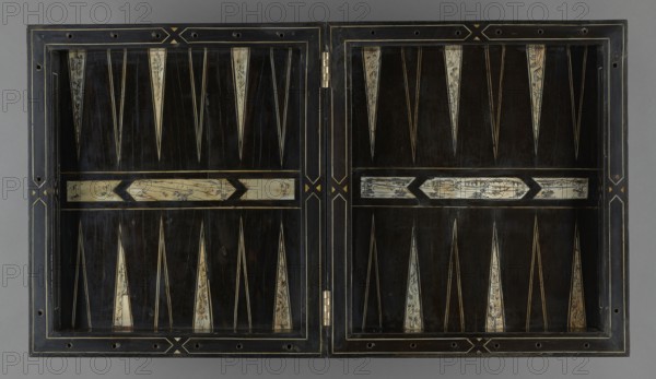 Chess, mill and backgammon box, games, flower vases, chess, plant decoration, baroque style, landscapes, backgammon, animals, birds, checkers party game, 1680s, France, furniture, equipment, game furniture, height 9 cm, width 37 cm, depth 32.8 cm, A rectangular hinged wooden board opened flat showing two panels with a symmetrical geometric pattern; the dominant color is dark brown to black in the field, with ivory-colored elongated triangular inlays and a few narrow pale lines creating pointed motifs; there are several horizontal pale rectangular inlays with darker decorative markings, and thin golden or yellow linear accents outlining panels and forming small diamond-like motifs near the center hinge; the outer frame is a darker wood with lighter edge lines and small circular holes along the border, and a metal hinge is visible at the center where the two panels meet.