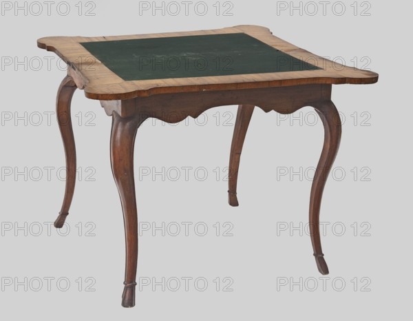 Game table, rectangular with an extendable top square when extended with rounded, protruding corners, supported by four cabriole legs ending in hoof-shaped feet. Foot stained walnut; top veneered in walnut with inlay. Rear frame two-part: outer composed of two rotating frames on wooden hinges with legs attached on the inner side supporting the foldable top plate. Outer side of the top framed by a crosswise frame with an asymmetrical, oval-shaped field, enclosed by channel bars and a ribbon, filled with floral and rocaille ornamentation. Inner side of tabletop has a wide walnut-veneered frame; center lined with green cloth. Function: game table / game furniture. Date: 1745–1770. Place of origin: Central Europe, possibly Saxony. Materials/technique: stained walnut, walnut veneer, inlay, green cloth. Dimensions: height 74.6 cm, width 95 cm, depth 49 cm., A wooden table with a rectangular top featuring an inset dark green panel, supported by a group of curved cabriole legs and a scalloped ...