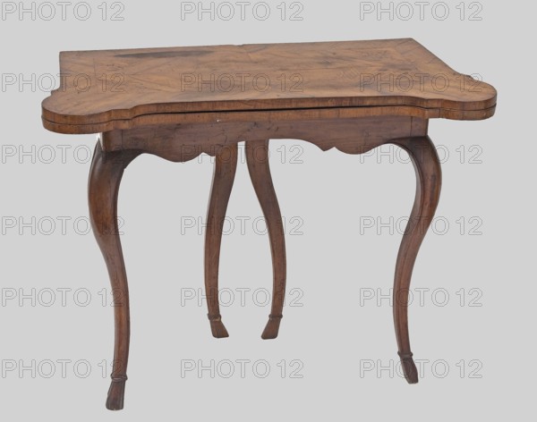 Game table, games, hooves animal legs, rectangular with an extendable top square when extended with rounded, protruding corners, supported by four cabriole legs ending in hoof-shaped feet. Foot stained walnut; top veneered in walnut with inlay. Rear frame two-part: outer composed of two rotating frames on wooden hinges with legs attached on the inner side supporting the foldable top plate. Outer side of the top framed by a crosswise frame with an asymmetrical, oval-shaped field, enclosed by channel bars and a ribbon, filled with floral and rocaille ornamentation. Inner side of the tabletop has a wide walnut-veneered frame; the middle is lined with green cloth. Dated 1745–1770, Central Europe, possibly Saxony. Furniture — game furniture, table. Height 74.6 cm; width 95 cm; depth 49 cm., A wooden small table with a scalloped rectangular top and curved apron supported by four cabriole legs. The wood shows varied brown tones with visible grain and darker brown streaks and spots; there are ...