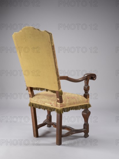 Armchair, neo-Baroque, padded seat and backrest, upholstered with large-patterned silk fabric, supported by four legs fastened with an H link; front legs baluster-shaped with a doll, rear legs angular and arched outward. Armrest supports are angular, profiled balusters; S-shaped armrests topped with a volute at the front. High backrest flared upwards, topped with a wavy crest, straight in line with the sitter's back. Upholstery fabric symmetrical, composed of stylized fleshy plant forms flowers, leaves, palmettes in cream on a red background; background has satin warp weave with pattern created by striking threads. Frame at the bottom and lower backrest finished with yellow silk fringe on a wide checkered ribbon; backrest sides and top finished with silver braid in a geometric pattern. Backrest interior finished with yellow cotton grosgrain. 2nd half of the 19th century, Italy, / Austria, seating furniture. Dimensions: height 121.5 cm, width 68 cm, depth 74 cm., The image shows the rea...