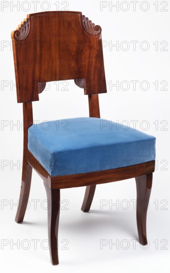 Chair, Biedermeier style, plant decoration, 1825–1840, possibly Warsaw or Vilnius, seating furniture chair, height 90.5 cm, width 46.8 cm, depth 50 cm, A wooden chair with a carved backrest in a warm brown finish and a blue upholstered seat cushion; the backrest shows carved scroll details near the top and small carved fan motifs near the lower edge; the seat cushion is a solid blue fabric with visible seams along the edges; the chair legs are wooden in the same warm brown tone, with slightly curved front legs and straighter back legs; the background is plain and light colored.