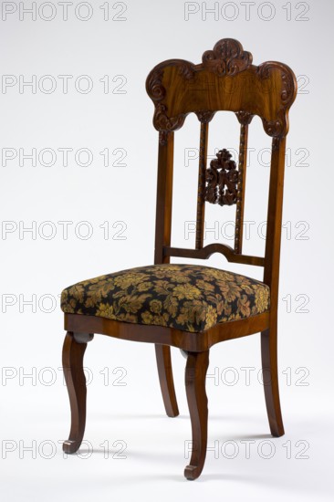 Chair, mahogany chair with a padded seat and a high openwork backrest, with carved decoration. Square legs, S-shaped at the front with volute feet, and arched rear legs. Wavy frame with rounded front corners, with a seat in the form of an overlay cushion. The backrest is framed on the sides by straight stiles extending the rear legs, topped with a board with a symmetrical, wavy-cut outline, emphasized by carved acanthus appliqués. The filling has two straight stiles covered with astragalus, topped and fastened together with acanthus leaf arrangements, and a narrow lower stile, arched between the stiles. Louis-Philippe style, acanthus ornament, plant decoration, dated 1850–1860, Poland, possibly Warsaw. Seating piece, height 118.5 cm, width 51 cm, depth 53 cm., A wooden chair with a carved backrest and ornate vertical supports, featuring a decorative carved motif in the center, a dark brown polished finish, and curved legs; the upholstered seat has a dark background patterned with a flo...