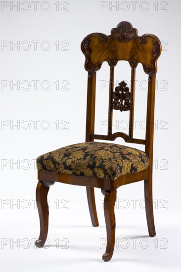 Chair, plant decoration, acanthus ornament, Louis Philippe style, mahogany chair with a padded seat and a high openwork backrest, with carved decoration. Square legs, S-shaped at the front with volute feet, and arched rear legs. Wavy frame with rounded front corners, with a seat in the form of an overlay cushion. The backrest is framed on the sides by straight stiles extending the rear legs, topped with a board with a symmetrical, wavy-cut outline, accentuated by carved acanthus appliqués. The filling has two straight stiles covered with astragalus, topped and fastened together with acanthus leaf arrangements, and a narrow lower stile, arched between the stiles. 1850–1860, Poland, possibly Warsaw. Piece of furniture, seating piece; height 118.2 cm, width 50.8 cm, depth 52.2 cm., A wooden chair with a carved top rail and decorative carved elements on the back, featuring vertical slats and a carved central ornament; the wood shows warm brown and darker brown grain tones. The upholstered ...