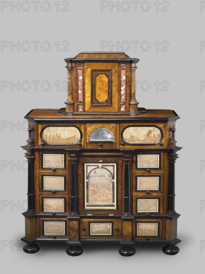 Cabinet, baroque style, columns, birds, early 18th century, Southern Germany, possibly Augsburg, piece of furniture, storage piece, height 114 cm, width 92 cm, depth 41 cm, A wooden cabinet with a layered, symmetrical design in warm brown and darker brown tones, accented with black trim and glossy black rounded feet; the upper section has a central rectangular raised compartment flanked by short columns with reddish-brown inlaid panels and lighter wood veneers, and the lower wider section features a central door with an arched framed panel showing a worn lighter wood scene, surrounded by paired dark columns and multiple small framed drawers on either side with lighter inset panels, plus a row of oval framed panels along the top front, all showing signs of age and wear and set against a pale grey background.