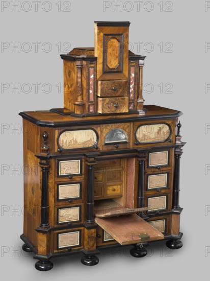 Cabinet, baroque, columns, birds, early 18th century, Southern Germany, Augsburg, piece of furniture, storage piece, height 114 cm, width 92 cm, depth 41 cm, A wooden cabinet with a warm brown finish and darker brown and black trim, featuring a stepped upper section with a central vertical panel and a pair of small drawers, flanked by narrow columns and panels with reddish accents; the midsection has a flat top surface and a row of decorative oval and arched panels above a recessed central compartment, which contains small wooden drawers and a pull-down shelf covered in worn red material with a brass latch, partially open; the lower section includes multiple small square drawers framed with dark trim on either side of the central opening, supported by turned black columns and resting on round black bun feet, with visible wood grain and areas of lighter tan and beige on several inset panels.
