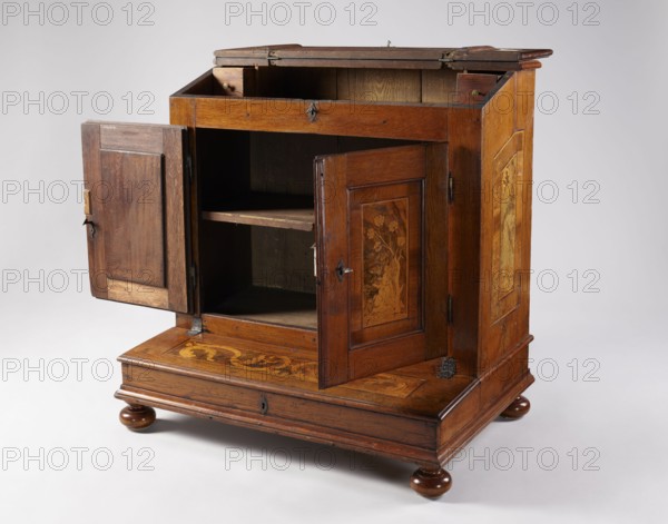 Kneeler, provenance unknown. Depicts Mary Magdalene Bible, Noli me tangere iconography, Jesus Christ Bible; used for prayer; Baroque style with ribbon ornament. Oak kneeler with a cuboid cabinet in the breastwork, hinged lid of the box base and a diagonally inclined lectern at the top; inlaid with plant motifs and genre scenes. Cabinet closed with double-leaf framed doors with panels attached at the back. Sides of the body, door, lid, and desk decorated with single fields repeating their outline, edged with veining and filled with inlaid motifs on a dark walnut background — on the doors a gardener by a rose bush, on the lid and desk wide O-shaped bands of acanthus leaves, and on the sides campanulas. One shelf inside the cabinet. Steel single-bolt applied door lock; brass French separable door hinges; steel lock plates in the form of a pointed oval; steel, slate-finished lid and desk hinges; door latch with a bolt attached to the left wing and a spring catch attached to the shelf. Date...