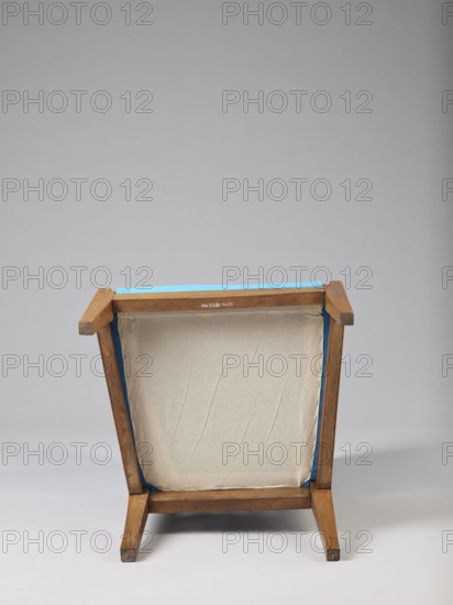 Armchair Berzera, armchair with a slender backrest and sides equal in height, arching upwards and forming ears, with angular frame elements. Front legs converge, rear legs arch outwards. Narrow, straight frame; trapezoidal seat in the form of a removable cushion on springs. The upper part of the sides and the backrest, which is slightly wider in the upper part, are upholstered; the lower part is filled with vertical slats. The frame elements are additionally connected with single pegs. Ca. 1820; possible origins: Warsaw, Vienna, Lesser Poland. Piece of furniture seating piece. Height 86.5 cm; width 54.8 cm; depth 61.8 cm., A wooden framed stool or small chair viewed from the back, showing a rectangular canvas or fabric panel stretched within the frame; the wood is light brown with visible grain and some darker worn spots, the fabric is off-white or beige with subtle creases, and there is a strip of bright blue trim or tape along the top edge and inner sides; the background is a smooth ...