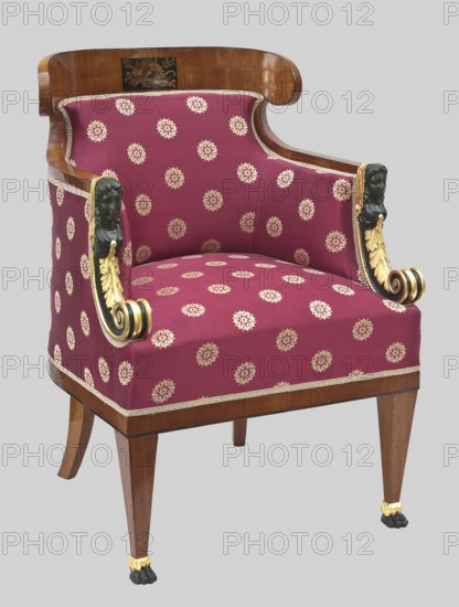 Armchair Berzera, plant decoration, female heads ornament, torches, roses, lion paws, arrows, Empire style, quivers. BERZERA–ARMCHAIR in the Empire type, mahogany, carved, upholstered. Square, tapered legs, arched at the back, straight at the front, terminating in feet in the shape of animal paws. Rounded back seat with spring upholstery; backrest arched in the line of the back, topped with a board with rounded corners; solid sides. The armrests are slightly recessed, in the form of an arched female herma with a volute at the bottom. The whole including the outside of the backrest and sides is upholstered with dark green velvet. 1815–1820, Warsaw. Piece of furniture, seating piece. Height 93 cm, width 63.5 cm, depth 60.5 cm., An upholstered armchair with a curved wooden back and wooden legs, covered in deep red fabric patterned with a repeating pale design; the chair has carved arm supports with dark sculpted faces and gilded scroll and leaf embellishments, gilt trim along the upholste...