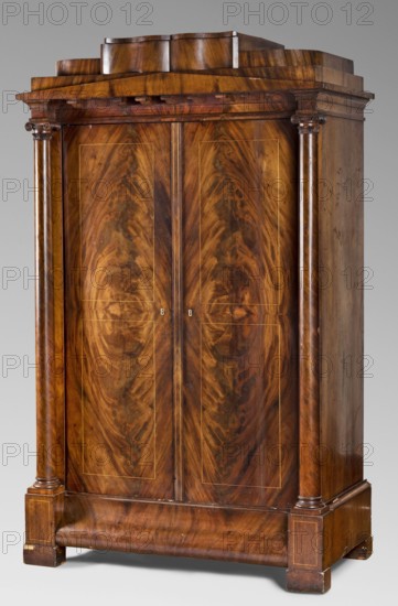 Wardrobe, Biedermeier style, architectural elements, columns, Biedermeier cabinet, mahogany, single-piece, with straight sides and front, closed by double doors framed by columns; with a triangular, flattened pediment and a drawer in a stepped finial; supported by low, block legs. The plinth is prominent, straight on the sides, profiled at the front with an S-shaped cross-section. The door leaves are rectangular, framed with light veining. At the front, below the pediment, are decorative corbels. The front corners of the stepped finial are rounded; the drawer face is wavy. Columns with smooth shafts, turned bases, and carved Ionic capitals. Four shelves on toothed rails inside. Board-shaped sides; frame-shaped back with two panels. Drawer bottoms are recessed. Single-bolt mortise door lock with brass front plate. Bone bookcases. 1830–1845, Berlin, storage unit, furniture. Dimensions: height 182.5 cm; width 110.5 cm; depth 58.5 cm., A large wooden wardrobe occupies the frame, showing a ...