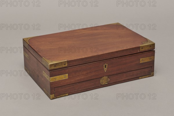 Painter's cassette, Travel painter's cassette, cuboid mahogany box with corners of body and lid reinforced with recessed brass sheets. At the bottom of the body a drawer is blocked by a brass pin inserted from above. Inside front: a row of compartments wider in the middle, square on the sides; behind them two removable containers — an upper one with five compartments three wide, separated by narrow ones and a lower flat container with round sockets for faience paint vessels. Includes a steel pen holder; nine paintbrushes three flat, six round, various numberings; makers include Pelikan and Z. Dudek Warszawa; five cylindrical glass containers; eight porcelain bowls signed Cmielów / MADE / IN POLAND; a set of watercolors 54 pans of various colors; a stick of black Chinese ink; and a resin stick. Bottom backed with green cloth. Inside the lid: a cardboard and red leather file folder closed with two small brass bolts. Mortise lock with two sliding hook bolts; brass lock plate in the form o...