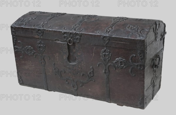 Chest, provenance unknown, plant decoration, flowers, Baroque style, wall-mounted chest, oak with side walls tapering towards the bottom and a convex lid, painted brown, reinforced and decorated with steel, openwork fittings in the form of plant twigs. The lid has three forged strips extending to the front wall and the strap hinges. The side edges of the lid are fitted with openwork bands, while the body is fitted with corners at the top and bottom. On the side walls are approximately oval handles mounted with strap fittings. The lock is a mortise-type lock from the front not preserved, with a latch mechanism and one bolt catch mounted in the lid, with an escutcheon framed by an openwork weave. The body walls are connected with exposed diagonal dovetails. The interior is lined with printed paper wallpaper floral pattern in the body, stripes in the lid. ca. 1750, Northern Germany, Poland, piece of furniture, storage piece, height 71.5 cm, width 129.5 cm, depth 64.5 cm, An old wooden che...