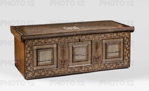 Chest, repossession provenance noted, geometric ornaments, plant decoration, vase ornament, chess, games. CHEST on a table base, inlaid with marquetry using the cerosine technique; cuboid with a flat lid bordered on three sides with moldings. Front divided into three squares by moldings. Entire piece carved in the massif, imitating frame-and-panel construction. Lid on both sides and the front richly decorated with veining and ornamentation. 16th century, Venice. Furniture; game furniture; storage furniture. Dimensions: height 45 cm, width 125 cm, depth 52.8 cm., A rectangular wooden chest with a hinged top, decorated with intricate inlaid geometric and floral patterns in contrasting light and dark tones; the wood appears brown with lighter cream-colored inlay forming repetitive star-like motifs and circular floral designs across the front panels and top, with carved framed panels and raised borders; the lid shows circular ornamental patterns and a central patterned square, while the fr...