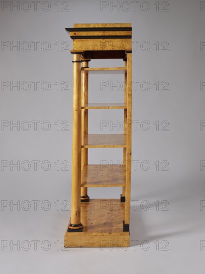 Shelf unit, columns architect, Biedermeier style, architectural elements, pilasters architect, birch, wall-mounted, with four rectangular shelves supported by four corner supports columns at the front, pilasters at the back mounted on a platform, supporting the profiled, architectural cornice of the upper wreath. Columns with smooth shafts. Plinths, bases, and capitals of the columns stained black. Shelves with a striped rim creating a kind of small, full gallery. Plate platform, on low block legs-pads, ca. 1830, Central Europe, piece of furniture for presenting objects, height 168 cm, width 105.5 cm, depth 49.5 cm, A tall wooden shelving unit photographed against a plain light gray background, showing a side view with a vertical column and a series of open shelves; the wood has a warm golden-brown tone with visible grain and darker brown knots, and there are small areas of black trim or accents on the column bases and shelf edges; the top has a slightly darker horizontal molding, and ...