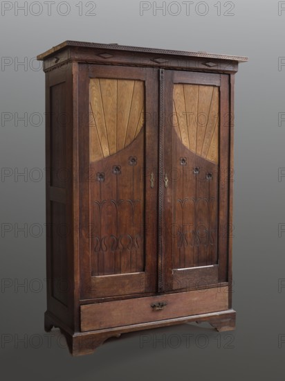 Wardrobe, vernacularism style, plant decorations, Zakopane style. A cubicle-shaped wardrobe in the Zakopane style, of carved oak, closed with double doors, with a drawer at the bottom, supported by four low console legs. Framed door leaves with single panels in the lower section engraved with stylized, elongated flowers, and with stave filling at the top creating a sun motif so-called rays. Framed sides and back with panels two and three; board drawer faces. Narrow crowning cornice, decorated with applied routins and corbels, and a zigzag pattern so-called gadzik. The cover strip is carved with a zigzag, a star, and stylized lilies so-called lilies. The whole was originally topped with a removable gallery attached with swivel tops. Inside, two hangers in the form of strips with peg hooks. Elongated brass lock plates, drawers with pull handles. Base door lock: espagnolette with brass plates; drawers: mortise, single-bolt, with brass plate. Early 20th century, Zakopane place of origin?, ...
