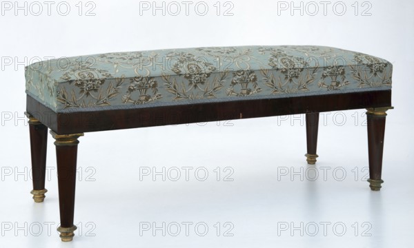 Banquette, empire style, early 19th century, rectangular mahogany banquette upholstered, supported by four turned, tapering legs with brass capitals and feet. Straight polished frame with cast, chiseled, gilded fittings. Spring-mounted upholstery. Height 52 cm, width 122.5 cm, depth 48 cm. Possible place of origin: Warsaw., A rectangular bench with an upholstered cushion covered in patterned fabric sits on a wooden frame with turned legs; the fabric shows floral and ornamental motifs in shades of pale blue, beige, gold, and cream, while the wooden frame and legs are dark brown with gilt accents on the leg caps and trim, set against a plain light background.
