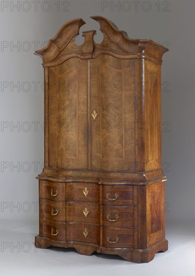 Sideboard, pre-war architectural elements, plant decoration. Two-part sideboard with chamfered and concave front corners, wavy front and straight sides; three-drawer base and top closed with double doors; supported on console legs. Veneered with patterned walnut, inlaid with ribbon motifs, polished. Tops of the upper section framed by richly profiled cornices, the upper one with a flat roof and a volute cornice with a central corbel. Top leaves have a wavy design creating a crossbow-like outline, mirrored by the narrow cornice above. Sides of both bodies, doors, and drawer faces are framed with a ribbon and cross-shaped frame. Three shelves not original inside. Construction of both bodies, drawer faces, and door leaves is board-like; back is framed with two panels; bases are board-like. Rims fastened to the sides with wedges. Steel applied locks; single-bolt drawer locks; double-bolt door locks. Steel pintle hinges; single-bolt steel-brass latches. Brass pull-style drawer handles. Bras...