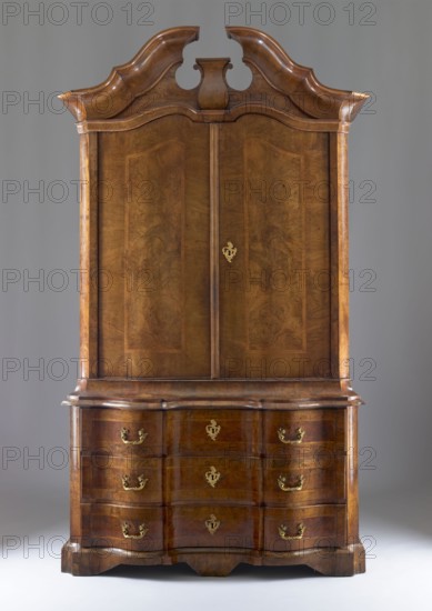 Sideboard, gift, architectural elements, plant decoration, two-part sideboard with chamfered and concave front corners, wavy front and straight sides, three-drawer base and top closed with double doors, supported on console legs; veneered with patterned walnut, inlaid with ribbon motifs, polished. The tops of the upper section are framed by richly profiled cornices, the upper one with a flat roof and a volute cornice with a central corbel. The top leaves have a wavy design creating a crossbow-like outline, as does the narrow cornice above them. The sides of both bodies, and the doors and drawer faces, are framed with a ribbon and cross-shaped frame. Three shelves not original are inside. Construction of both bodies, drawer faces, and door leaves is board-like; the back is framed with two panels; bases are board-like. Rims fastened to sides with wedges. Steel applied locks; single-bolt drawer locks; double-bolt door locks. Steel pintle hinges; single-bolt steel-brass latches. Brass pull...