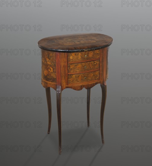 Chest of drawers table, classicism and rococo styles, floral decorations. Oval chest with a tall body containing three drawers, supported by four slender S-shaped legs, richly inlaid. Body is wavy-cut at the bottom. Wooden top with a wide rosewood frame and quadruple veneer; oval field filled with a heraldic composition central coat of arms with a palm tree supported by standing lions, against a cloak suspended from two open five-stick crowns and flanked by a pair of Indians in plumes. Edge of the tabletop is rounded and blackened. Drawer handles are brass knobs. 4th quarter of the 19th century, Central Europe. Piece of furniture storage. Height 75.24 cm; width 50.1 cm; depth 34.4 cm., A small wooden oval-topped table with a dark brown top and lighter brown body stands on four slender curved legs in a darker brown. The front and sides of the body show decorative floral inlays in shades of brown and golden brown. The table has a scalloped apron beneath the body and a few round metal-col...