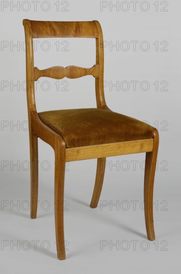 Chair, furnishings of representative buildings of the Republic of Poland 1918–1939, Biedermeier style, klismos. CHAIR with a trapezoidal padded seat removable cushion, rectangular openwork backrest filled with a wavy-cut crossbar; supported by sabre-shaped legs, the rear ones passing into the backrest stiles. The side frames, S-shaped, connected to the front legs and the side stiles of the backrest, frame the seat; the front and rear frames, straight, placed below the side stiles, support the cushion. 1820–1840, Warsaw; seating furniture, piece of furniture. Height 86.5 cm, width 44.3 cm, depth 44.5 cm., A wooden chair with a curved backrest and a carved horizontal slat, a padded seat upholstered in a brownish-golden fabric, gently tapered legs with a light to medium wood grain finish, and a plain neutral background in shades of light gray; visible colors include brown, golden-brown, light wood tones, and gray.