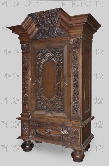Wardrobe, provenance, putti; baroque; coats of arms; plant decoration; lion masks; personifications of the Seasons: Spring, Summer, Autumn, Winter; 1710–1730; Gdansk, Royal Prussia; piece of furniture storage; height 200 cm, width 124 cm, depth 62 cm, A large ornate wooden cabinet stands against a light gray background, carved from dark brown wood with rich grain. The cabinet features an overhanging cornice with stepped molding and an elaborately carved crest with floral and foliate motifs. The central door has a recessed panel with symmetrical carved ornamentation including curved arch shapes and foliate scrollwork, flanked by vertical carved pilasters with leafy relief. The lower section includes a broad rail and a carved drawer front with geometric and floral carvings, supported by round bun feet in polished dark brown. Overall tones visible are dark brown wood with areas of lighter brown highlighting the grain, and the background is light gray.