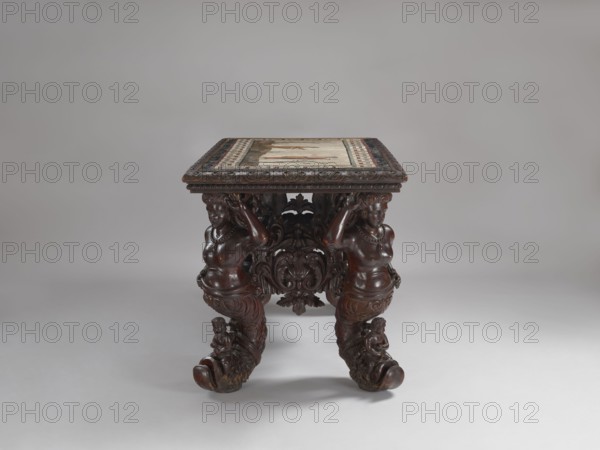 Table, Neo-Baroque, richly carved table with a rectangular mosaic top supported by four supports in the form of caryatids transforming into dolphins at the bottom, connected by an openwork frame. The frame on the long sides consists of an acanthus coat-of-arms cartouche held by a pair of mermaids; the side frames are composed of an acanthus cartouche and an acanthus twig with flowers. On the dolphins, which serve as the feet of the legs, sit putti in loincloths. Nude female figures, with corals around their necks, support the tabletop with their right hand, left hands resting on their hips. The mosaic is set into the tabletop with a profiled carved border a braid with a plant twig; the figurative scene is framed by a wide border with a meander. On the left, a woman kneeling on her left knee with a branch in her left hand; on the right, a man in a tunic, with his right hand raised and a spear in his left. The composition is decorated in shades of gray, blue, and beige with brown. The fo...