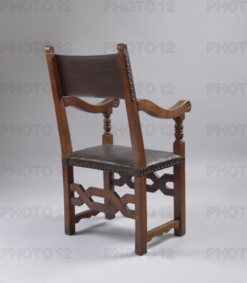 Armchair, ARMCHAIR with a frame composed of simple, angular elements, with a seat and backrest upholstered in leather. The legs are held together by a box-like binding composed of narrow joins on the sides and wide geometric wattles on the front and back. Rectangular seat, upholstered on straps. The backrest is composed of side rails and a piece of thick leather nailed with headstocks in their upper section, above the armrests; tilted. The armrests are S-shaped, topped with volutes at the front, on turned supports in the form of a baluster, constituting, like the backrest rails, an extension of the legs. The volutes at the top of the backrest stiles are carved with acanthus leaves, while the outer and inner sides of the armrest volutes are decorated with rosettes. The frame elements are accentuated around the perimeter with a delicate groove, and their tenon joints are pegged. Baroque style, wattle and rosette ornament, acanthus ornament, balusters. 1st half of the 17th century. Possib...