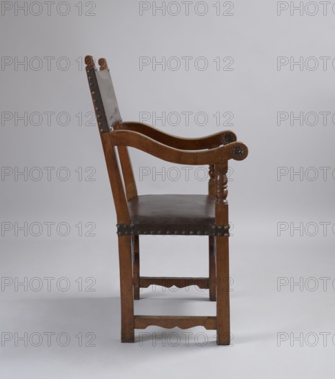 Armchair, wattle ornament, rosettes ornament, acanthus ornament, balusters, Baroque style. Armchair with a frame composed of simple, angular elements, with a seat and backrest upholstered in leather. The legs are held together by a box-like binding composed of narrow joins on the sides and wide geometric wattles on the front and back. Rectangular seat, upholstered on straps. The backrest is composed of side rails and a piece of thick leather nailed with headstocks in their upper section, above the armrests; tilted. The armrests are S-shaped, topped with volutes at the front, on turned supports in the form of a baluster, constituting, like the backrest rails, an extension of the legs. The volutes at the top of the backrest stiles are carved with acanthus leaves, while the outer and inner sides of the armrest volutes are decorated with rosettes. The frame elements are accentuated around the perimeter with a delicate groove, and their tenon joints are pegged. 1st half of the 17th century....
