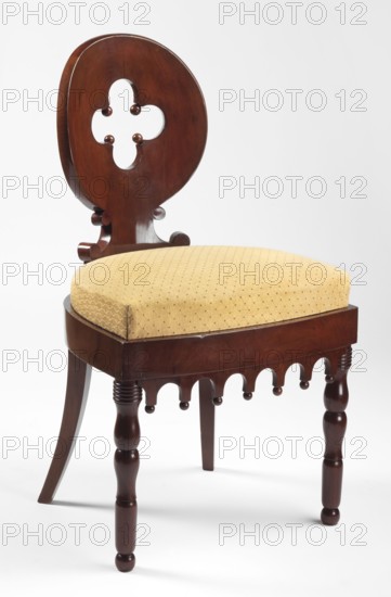 Chair, Biedermeier and Gothic Revival styles, mahogany chair with a removable padded seat cushion and a boarded oval backrest featuring a central quatrefoil openwork. Front legs straight, turned in a baluster form; rear legs angular, tapering, arched outward. Seat rounded at the back, bulging at the front. Frame straight, glued from two layers of squared timbers in a brick pattern; front apron with semicircular arcades and balls at the bottom. Backrest curved to follow the back, mounted on a support with C-beam side supports. Originally a cushion on a pine frame, upholstered in green velvet; currently in a yellow fabric with a geometric pattern. Dated 1815–1830, Poland. Seating furniture, height 84 cm, width 48 cm, depth 48.8 cm., A wooden chair with a dark brown polished finish and a rounded backrest featuring a cutout quatrefoil shape, a cushioned seat upholstered in a yellow patterned fabric, turned front legs and a slightly curved rear leg, and decorative scalloped apron details be...