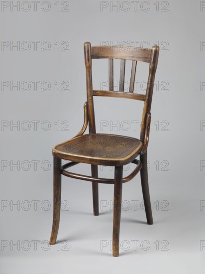 Chair, Johann Kohn & Cie bentwood furniture factory, Radom; late 19th century?–1939. BENTWOOD CHAIR with an openwork backrest and a trapezoidal seat made of extruded plywood with rounded corners. Profiled, straight front legs, slightly diagonally inclined at the bottom; rear legs arch outward, merging into the sideways-flared backrest frames. Legs are joined at the top with a hoop repeating the outline of the seat. U-shaped connectors between the backrest frames and the seat frame. The backrest has two horizontal slats bent in the back line, the upper one wider, with three slats between them. Circa 1900–1914, Radom. Seating furniture; height 89.5 cm, width 39.5 cm, depth 49 cm., A wooden chair with a curved backrest and three vertical slats is shown against a pale gray background, the chair displaying a dark brown finish with lighter worn areas, a carved or embossed decorative pattern on the seat, gently tapered front and back legs, rounded supports connecting the legs, and a slightly ...