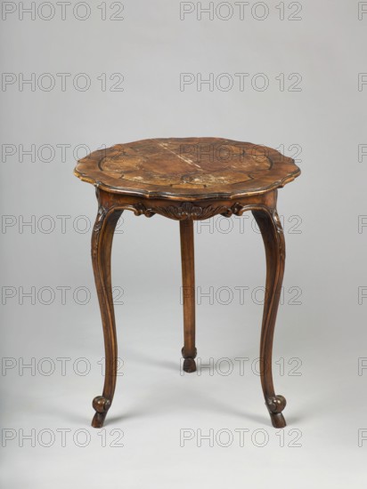 Table, rococo style with shell ornament, plant decorations, ROUND neo-rococo table, carved and inlaid, supported by three S-shaped slender legs. Legs terminate at the bottom with volutes and hooved feet, at the top arched to a wavy-cut frame. Center of each frame has a shell cartouche with acanthus tendrils and flowers; bottoms have half-rounds forming channel sections connected by volutes. Tabletop edge has a quarter-round profile with a step, cut with many leaves. Center of tabletop bordered with a wattle-and-daub pattern of light and dark ribbon-and-pincer motifs, framed crosswise on the outside; center filled with patterned walnut, frame is smooth walnut, wavy fields made of poplar burl. Dated 1880–1900. Origin possibly Poland or Germany. Furniture, table; height 71.5 cm, diameter 58.8 cm., A wooden round table with a scalloped edge top showing natural wood grain and worn finish sits on three curved cabriole legs with carved floral and scroll details; the wood tones range from medi...