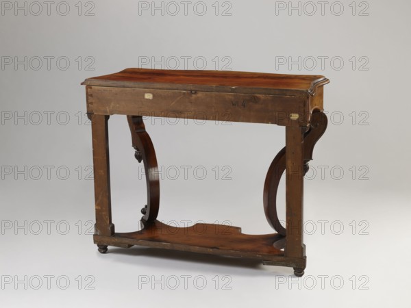 Console, Biedermeier and Louis Philippe styles, carved mahogany-veneered console on four angular legs mounted on a platform with a wavy outline; front legs strongly curved, rear legs straight, flattened, with bases and capitals. Entire piece polished. Platform supported by four low turned legs. Lower section of legs composed of channel sections decorated at top and bottom with knobbed pinnacles. Wide frame repeats concave–convex shape of top, rounded at front corners, wavy-cut at bottom, framed with a half-cylinder; front frame forms face of drawer. Top has a profiled edge, connected to frame with cube side panels. Drawer contains two rows of compartments inside; small front corner compartments have rosewood covers. Drawer secured by a single-bolt mortise lock. Dated 1835–1850. Piece of furniture table. Height 82 cm, width 107.2 cm, depth 45 cm., A wooden table displayed against a neutral light gray background, showing a rectangular top with a warm reddish-brown surface and a slightly ...